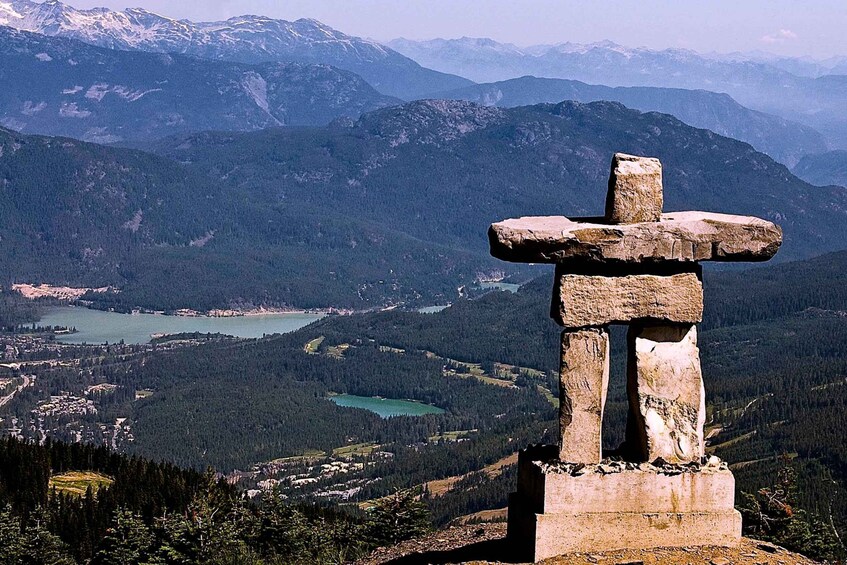 A stone totem pole in a mountainous landscape with a lake and forested valley. 1