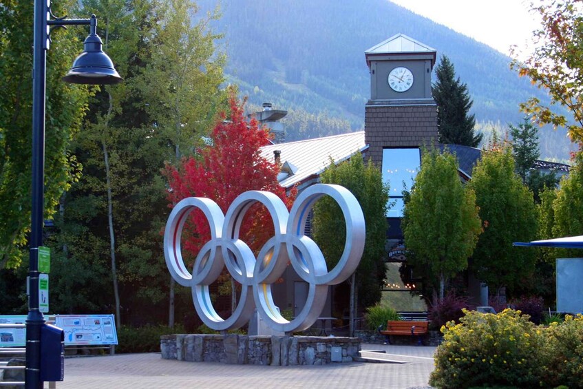 A large Olympic rings sculpture in front of a building with a clock tower. 2