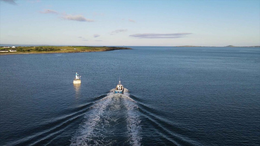 A boat moving across a calm sea with a lighthouse in the distance and a shoreline with buildings. 1
