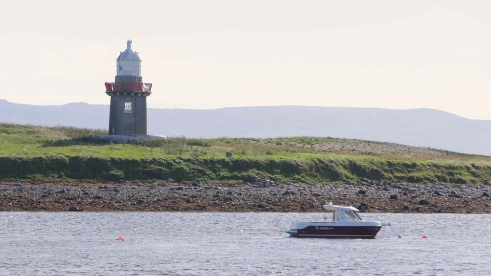 A lighthouse on a grassy hill by the water with a boat in the foreground. 2