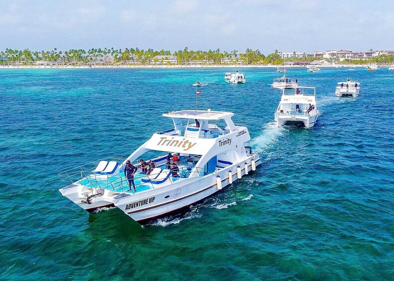 Una embarcación blanca llamada 'Trinity' con la leyenda 'Adventure VIP' en la parte trasera, navegando sobre aguas azules y cristalinas, con otras embarcaciones al fondo. 5