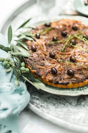 A savory tart with caramelized onions and black olives, garnished with herbs, on a ceramic plate. 3