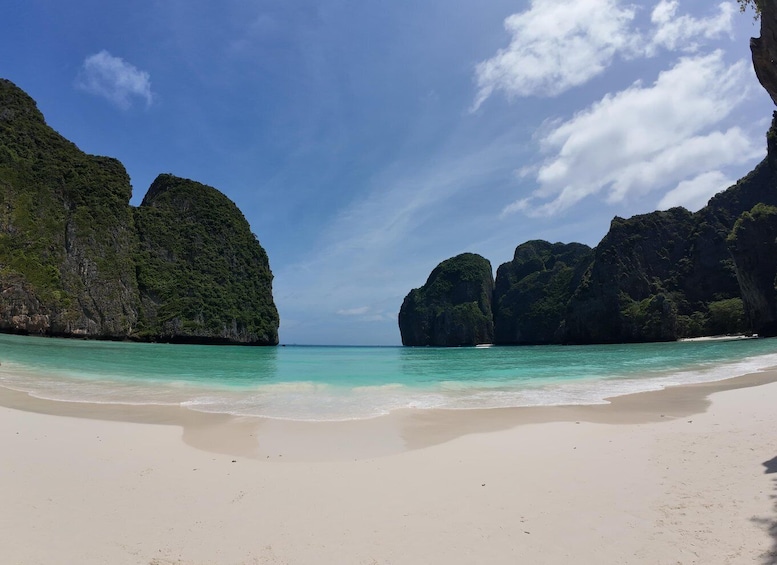 A beach with clear turquoise water, white sand, and large green rock formations. 3