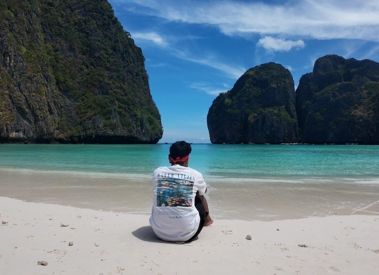 A person sitting on a beach facing large rock formations. 1