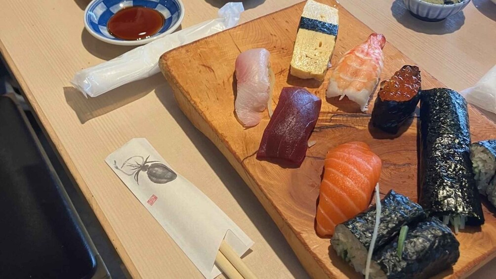A wooden sushi platter with various types of sushi and a small bowl of soy sauce. 3