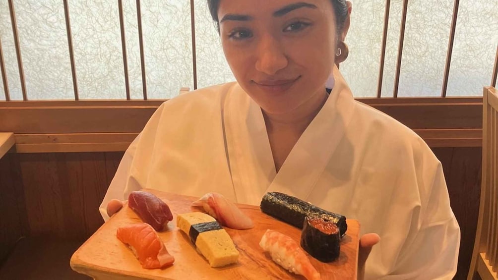 A person in a white robe holding a wooden tray with sushi. 1