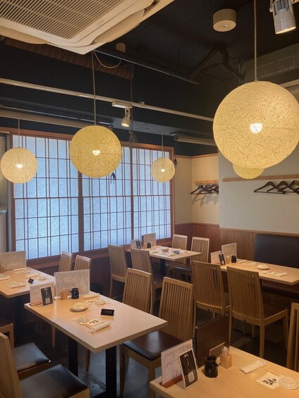 A restaurant interior with round, textured hanging lights, wooden tables, and chairs. 2