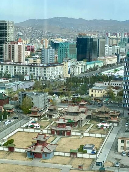 A cityscape with modern high-rise buildings, traditional architecture, and a mountainous backdrop. 5
