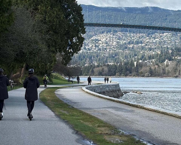 A paved path alongside a river with a bridge in the background. 2