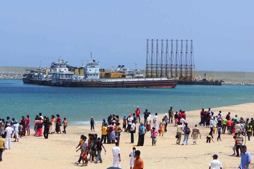 Ein überfüllter Strand mit einem großen Schiff im Hintergrund. 1