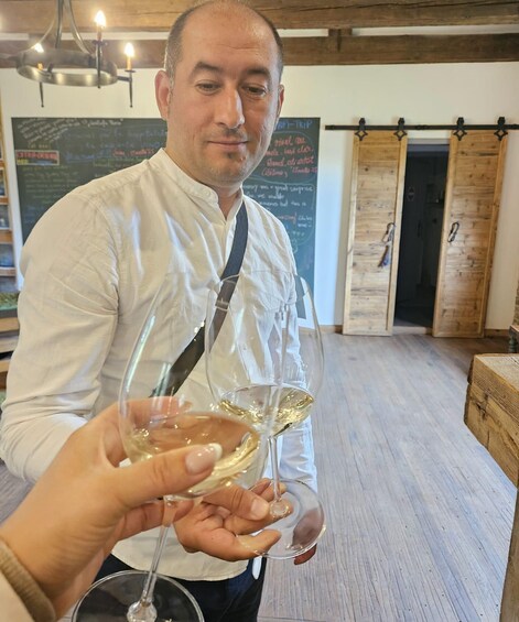 A person holding two wine glasses in a rustic interior with wooden doors and a chalkboard menu. 5
