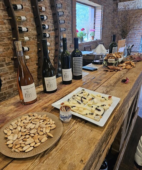 A wooden table with wine bottles, cheese, almonds, and bread. 2