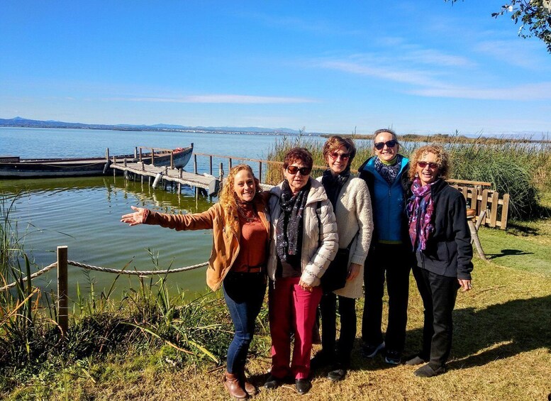 A group of people standing by a lake with a dock and boats in the background. 3