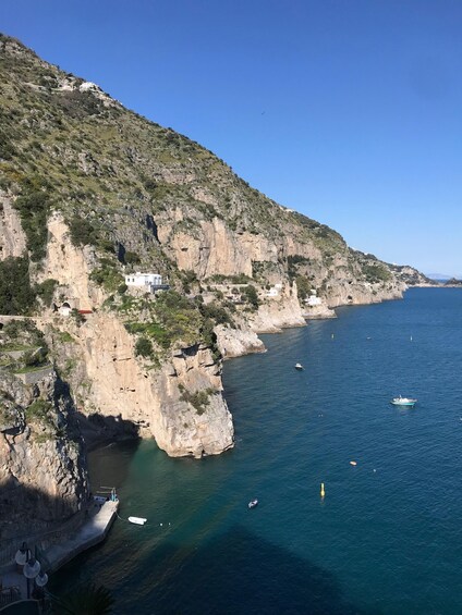 A coastal cliff with buildings, a clear blue sea, and boats. 5