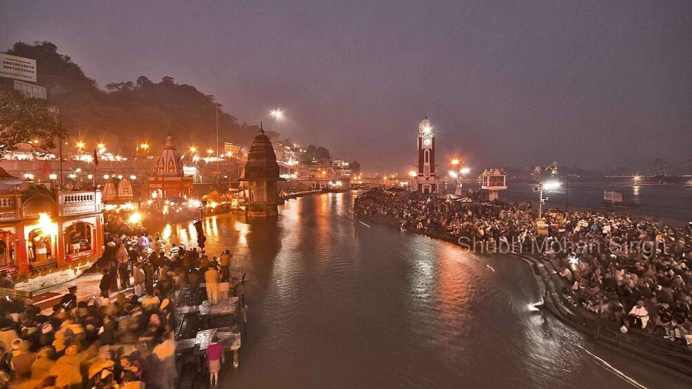 Un río con gente reunida en sus orillas, un puente y edificios iluminados. 1