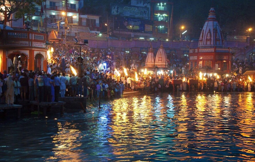 Un río con reflejos de luces y una multitud reunida alrededor de un templo con aguja. 4