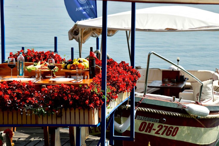 A boat with a table laden with fruits and vegetables, a bottle of wine, and a sign reading 'passengers OH-2760' against a backdrop of water and a clear sky. 3