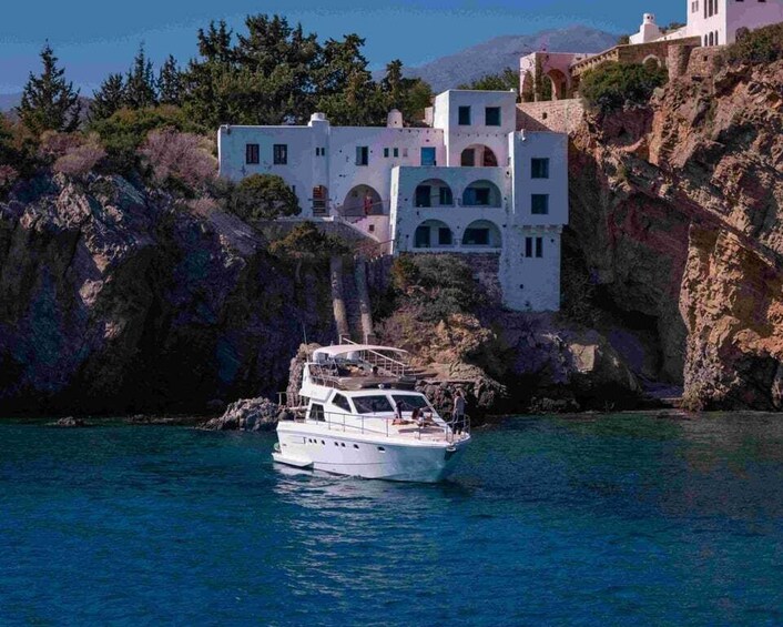 A white yacht on calm blue waters, a white building with arches on a rocky cliff, and a mountainous backdrop. 3