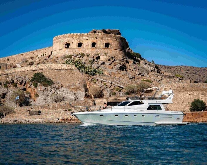 A boat on calm water, a historic stone fort on a hill, and a clear blue sky. 1