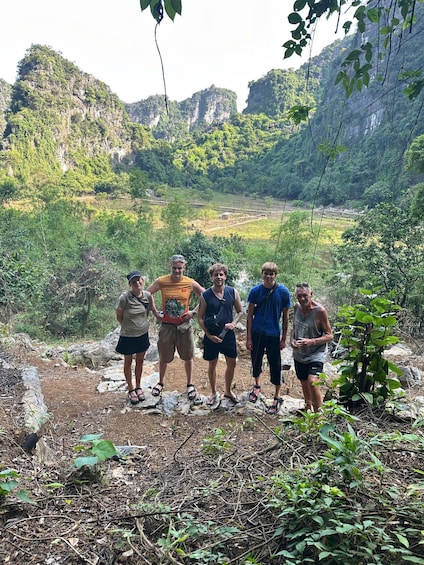 A group of people standing on a rocky path surrounded by lush greenery and mountains in the background. 1