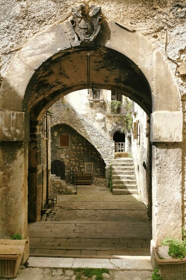 An ancient stone archway leading to a narrow street with steps and a building in the background. 4