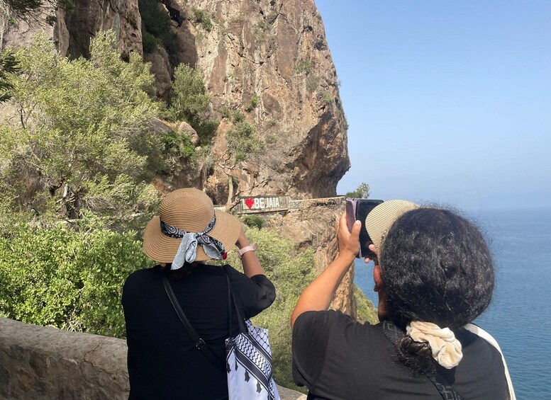 Two people taking a photo of a cliff with a sign that says 'I BEJIA'. 3