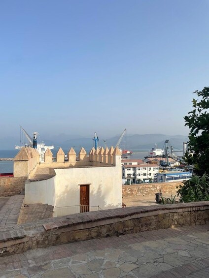 A coastal town with a fortified structure, a harbor with ships, and a distant mountain range. 2