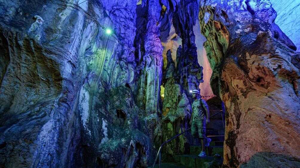 A cave with stalactites and stalagmites, a person climbing a rope ladder, and a helmet on the ground. 2