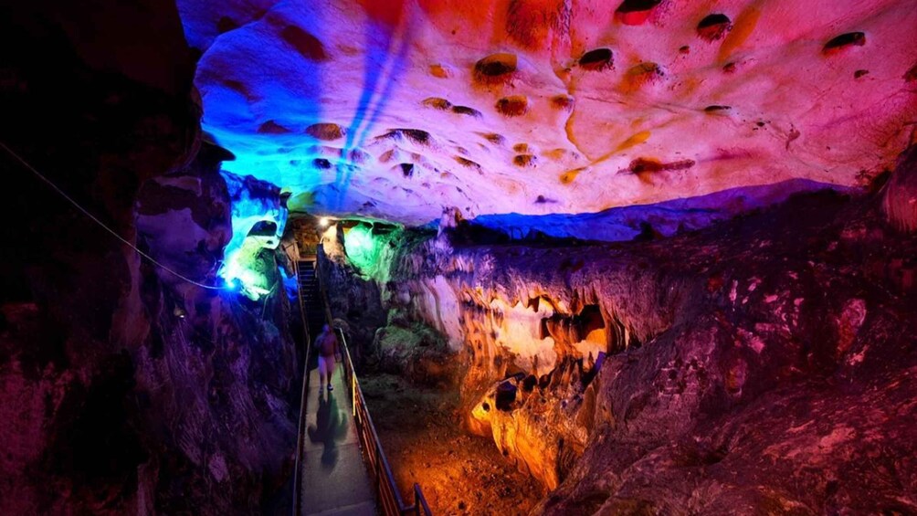 A cave illuminated with colorful lights, a narrow passageway, and stalactites. 3