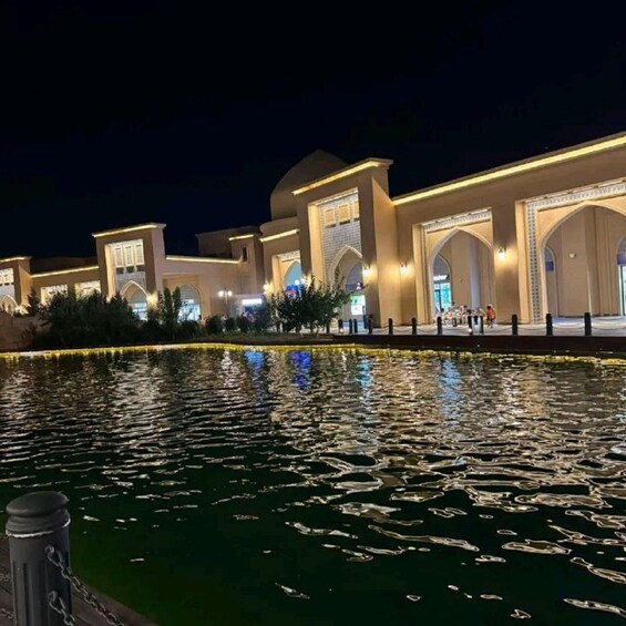 A well-lit building with arched windows and a reflective water body in front. 5