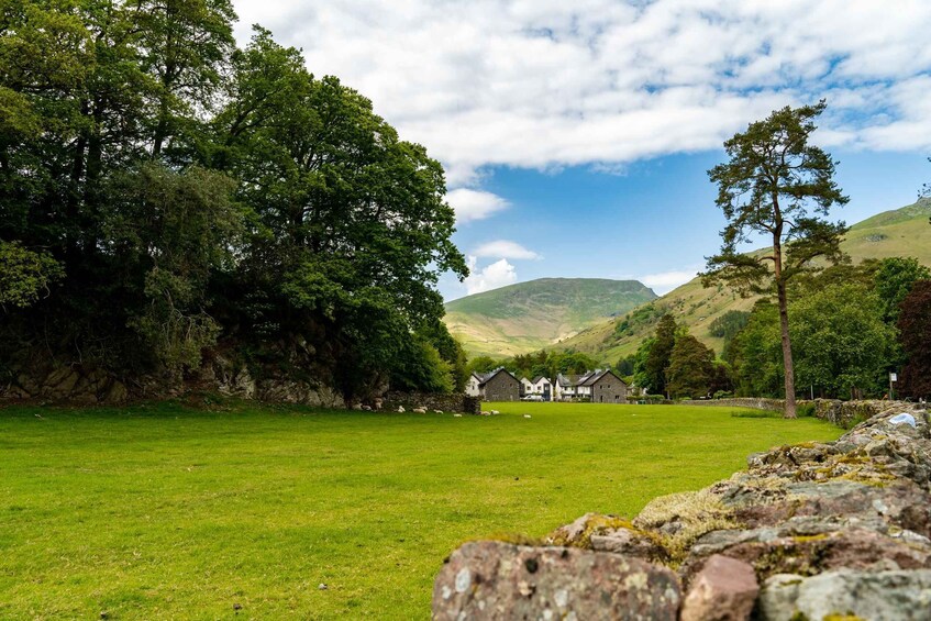 A grassy field with stone walls, a row of houses, and a hill in the background. 1