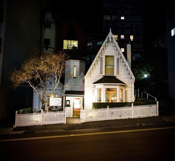 A Gothic-style building with a white picket fence, a tree, and a lit signboard. 4