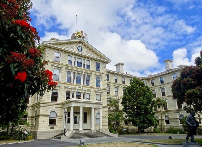 A large, historic building with a clock tower, surrounded by lush greenery and a statue. 2