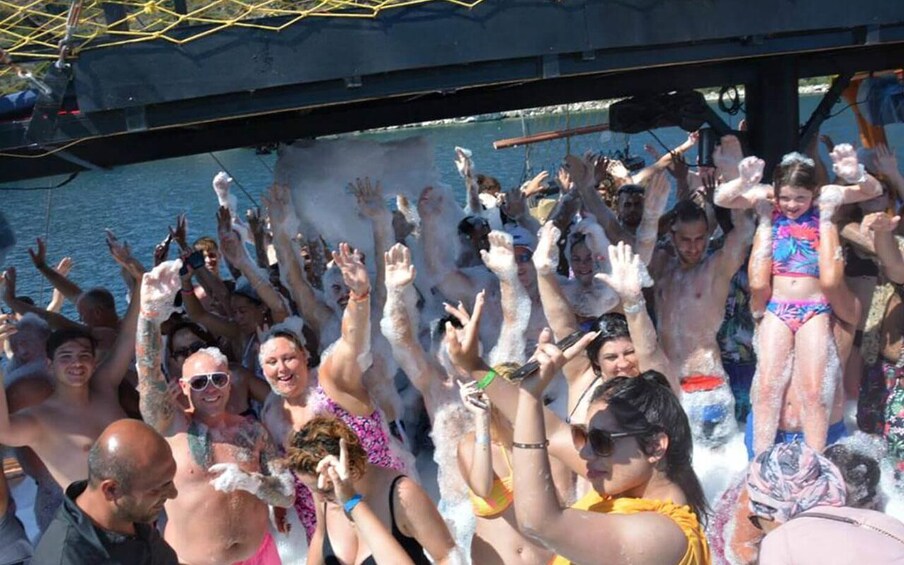 A group of people on a boat, some covered in foam, with a body of water and a dock in the background. 4
