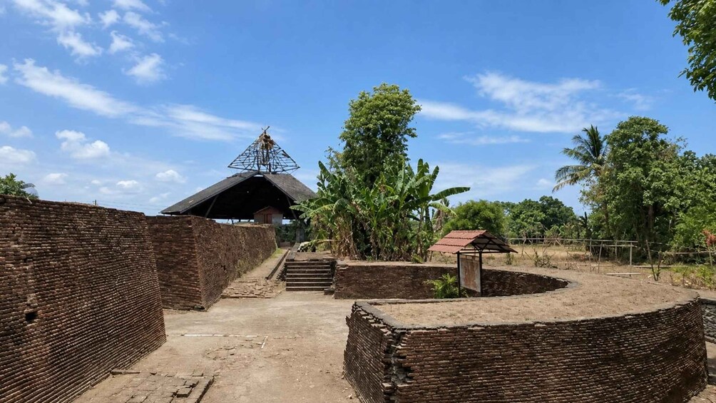 A historical site with brick walls, a thatched-roof building, and a satellite dish. 3
