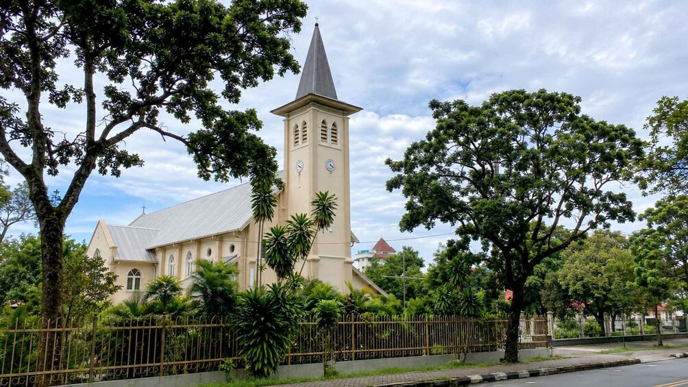 A church with a tall steeple and clock, surrounded by trees and a fence. 5