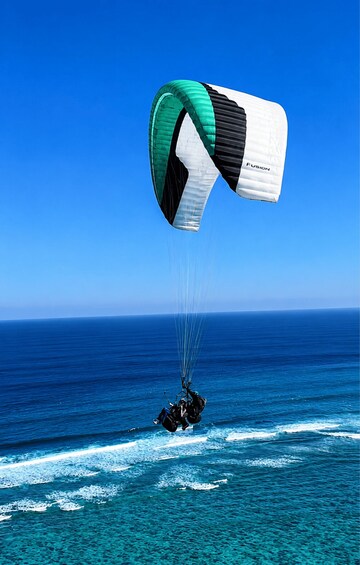 A paraglider with a green and white parachute over the ocean. 3