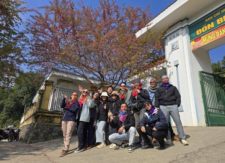 A group of people posing in front of a building with a sign that reads 'BAN CHI HONG BANG' and 'MÜNG DÂN.' 5