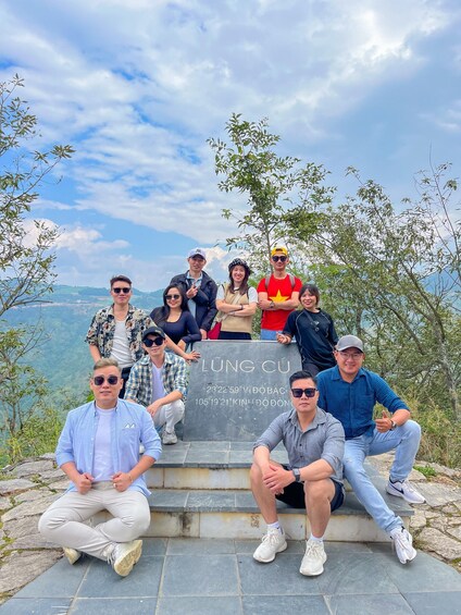A group of people sitting on stone steps with a sign that reads 'LUNG CU' and coordinates '23°22'59.59' N 105°19'21.00' E' in the background. 4