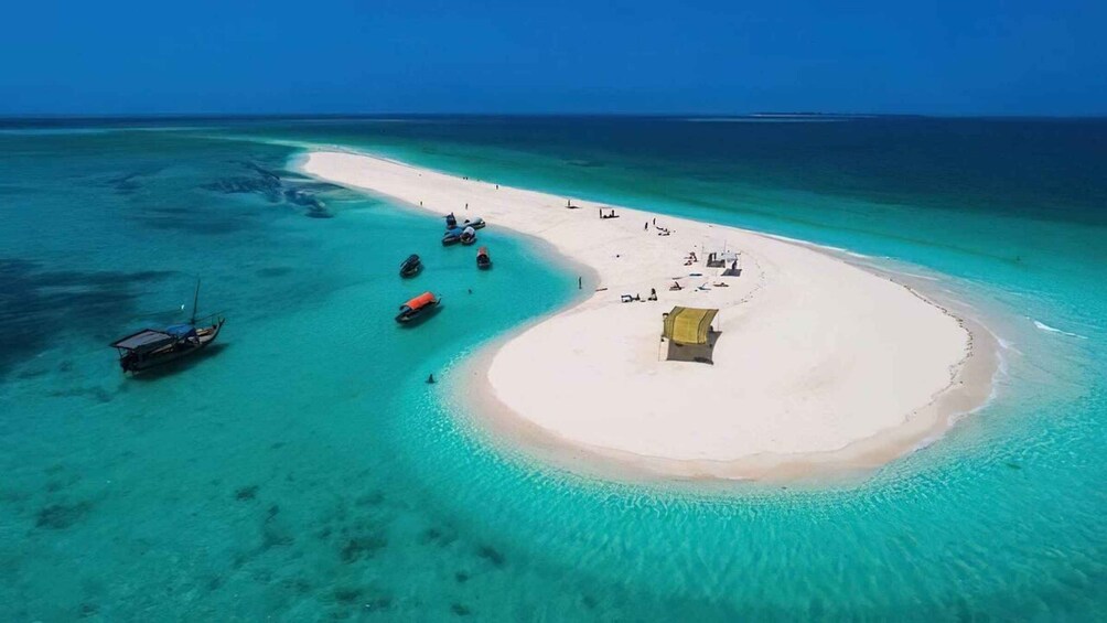 A turquoise beach with a small island, clear waters, and a boat anchored near the shore. 1