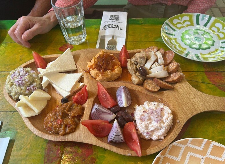 A wooden board with various cheeses, olives, and pickled vegetables. 2