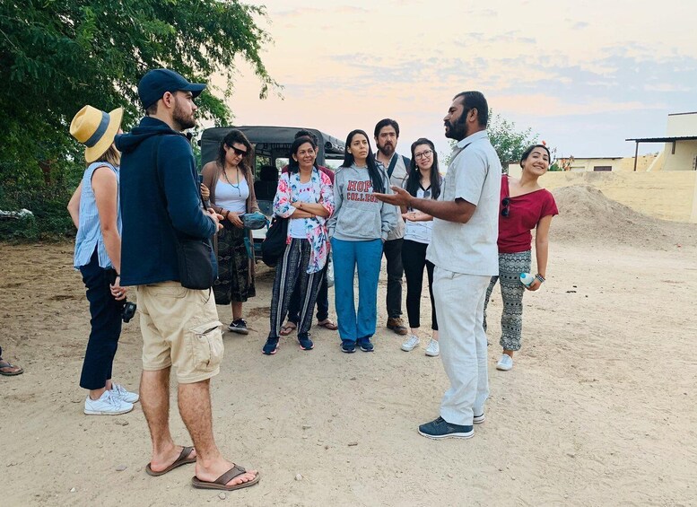 A group of people standing outdoors in a sandy area with trees and a building in the background. 1