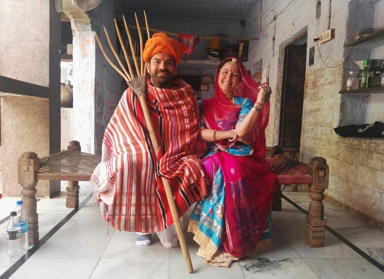 A man and a woman sitting on a bench in a traditional setting, with a fan and wooden sticks in the background. 4