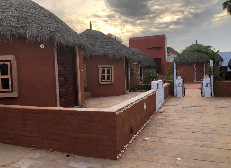 Traditional mud-brick houses with thatched roofs, a paved walkway, and a red building in the background. 2