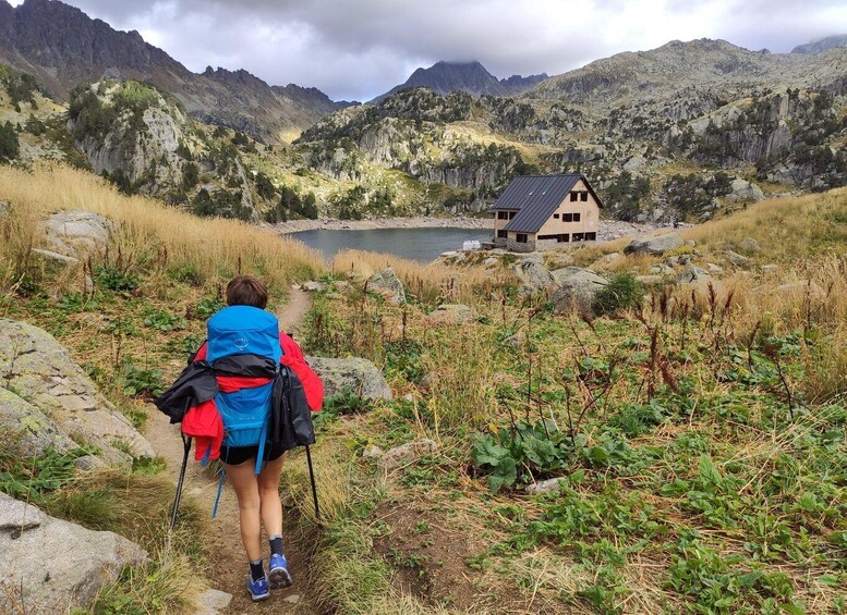 A hiker on a trail with a mountain backdrop and a house by a lake. 5