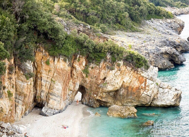 A coastal landscape with a rocky cliff, a beach, and clear turquoise waters. 1