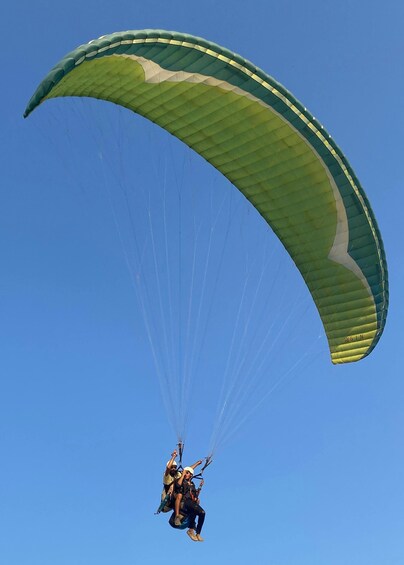 A person paragliding with a green and white parachute against a clear blue sky. 3