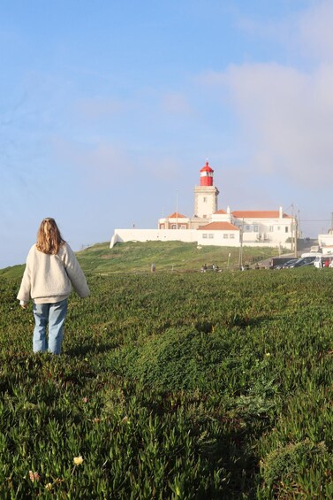 Una persona cammina su una collina erbosa verso un faro. 4