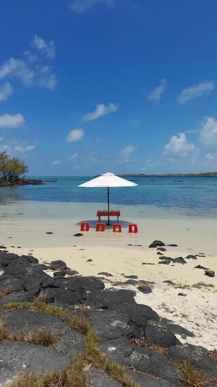 Een strand met een witte parasol en rode stoelen. 3