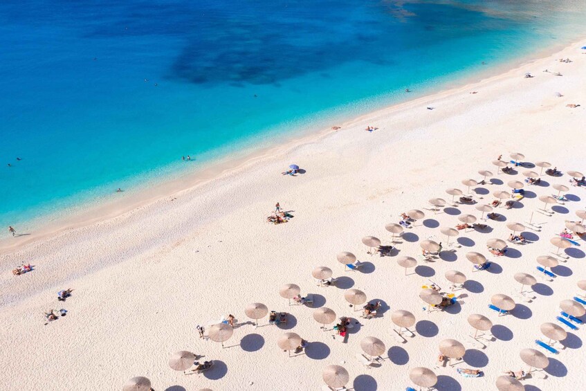 A beach with clear turquoise water, sandy shore, and numerous umbrellas and lounge chairs. 2